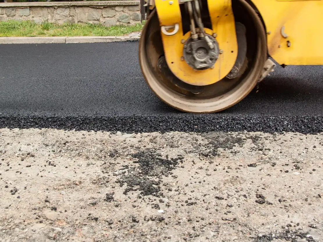 Roller drum compacting the edge of a fresh asphalt mat