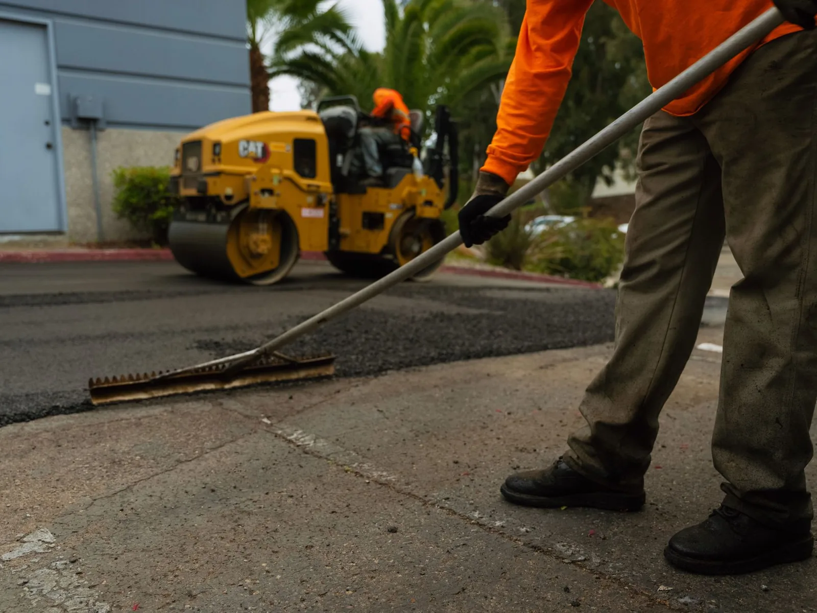 Worker raking the hot mix edge of new asphalt as a roller follows, asphalt driveway paving