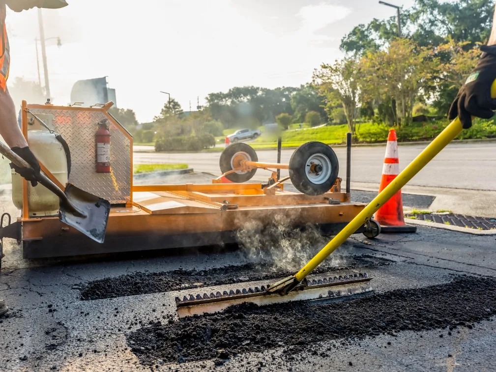 Crew raking steaming hot mix into a pothole patch, asphalt repair
