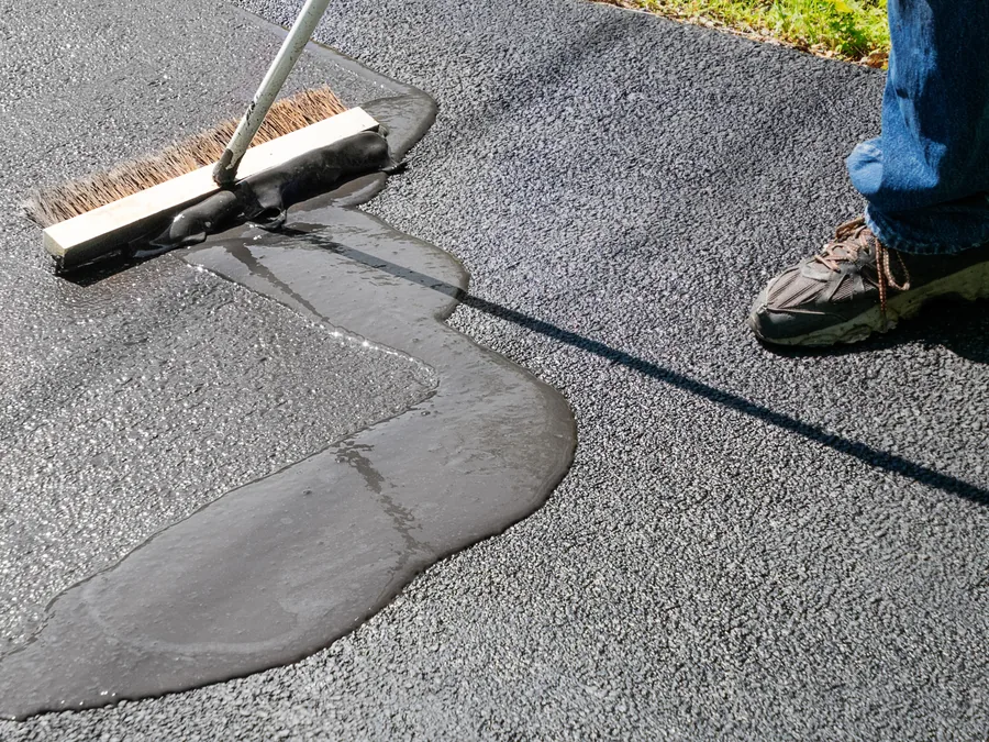Broom spreading fresh sealer over a filled crack, asphalt sealcoating