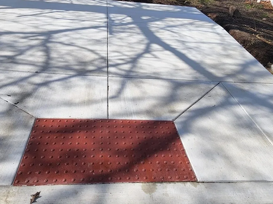 New concrete sidewalk ramp with a red detectable warning pad, concrete contractor work