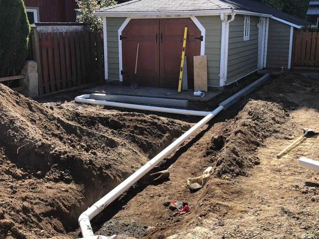 White drain pipe laid in an open trench across a backyard, grading drainage work
