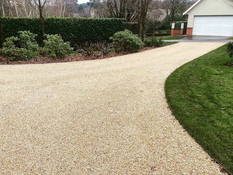 Fresh gravel driveway curving between lawn and shrubs to a garage, gravel driveways