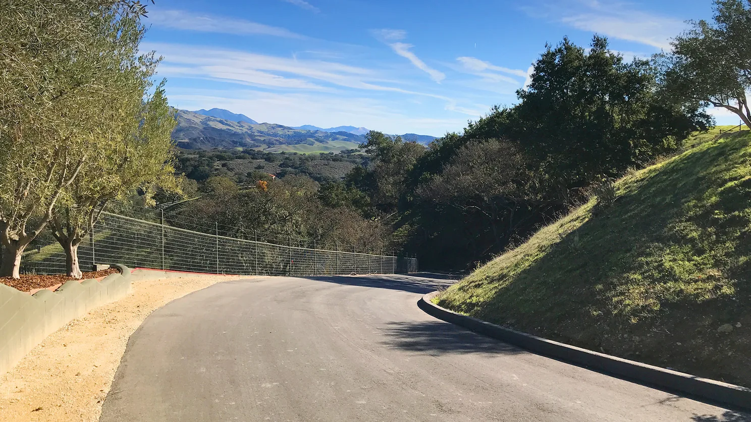 Fresh asphalt paving on a private drive curving toward tree covered hills