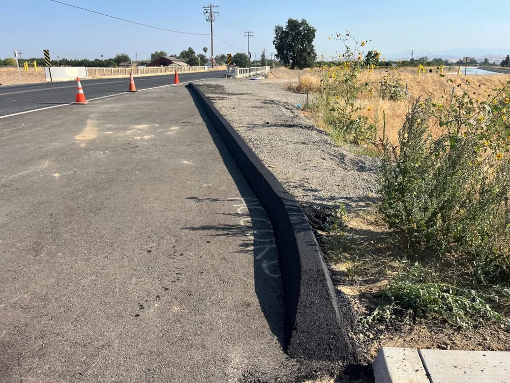 New asphalt berm along the edge of a rural road with dry grass, private road paving