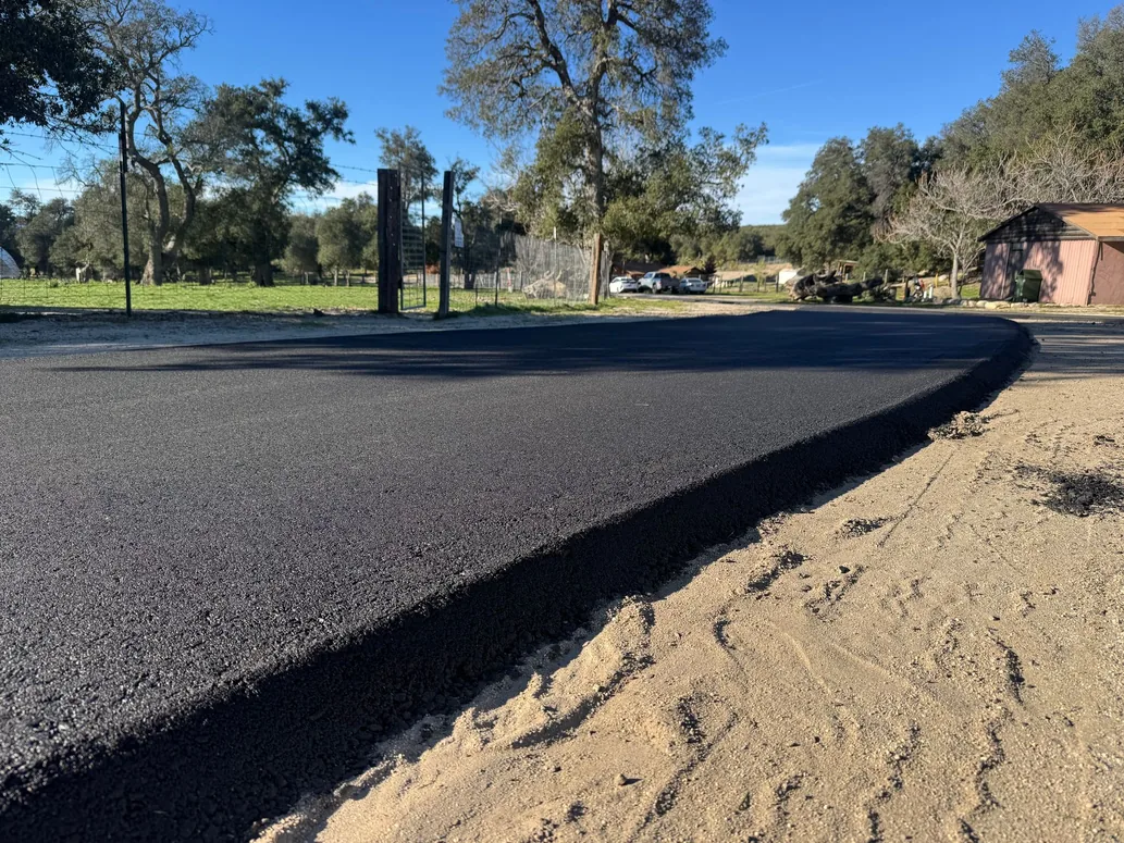 Fresh asphalt edge and sand shoulder of a new road under shade trees, private road paving
