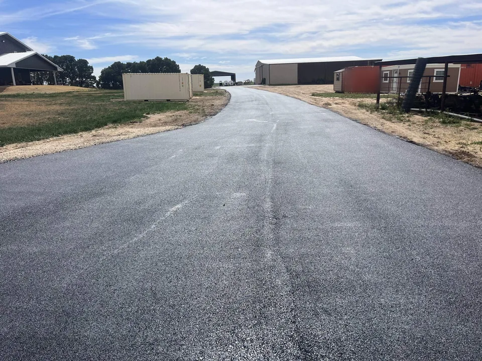 New asphalt road running past barns and storage buildings on a rural property, private road paving