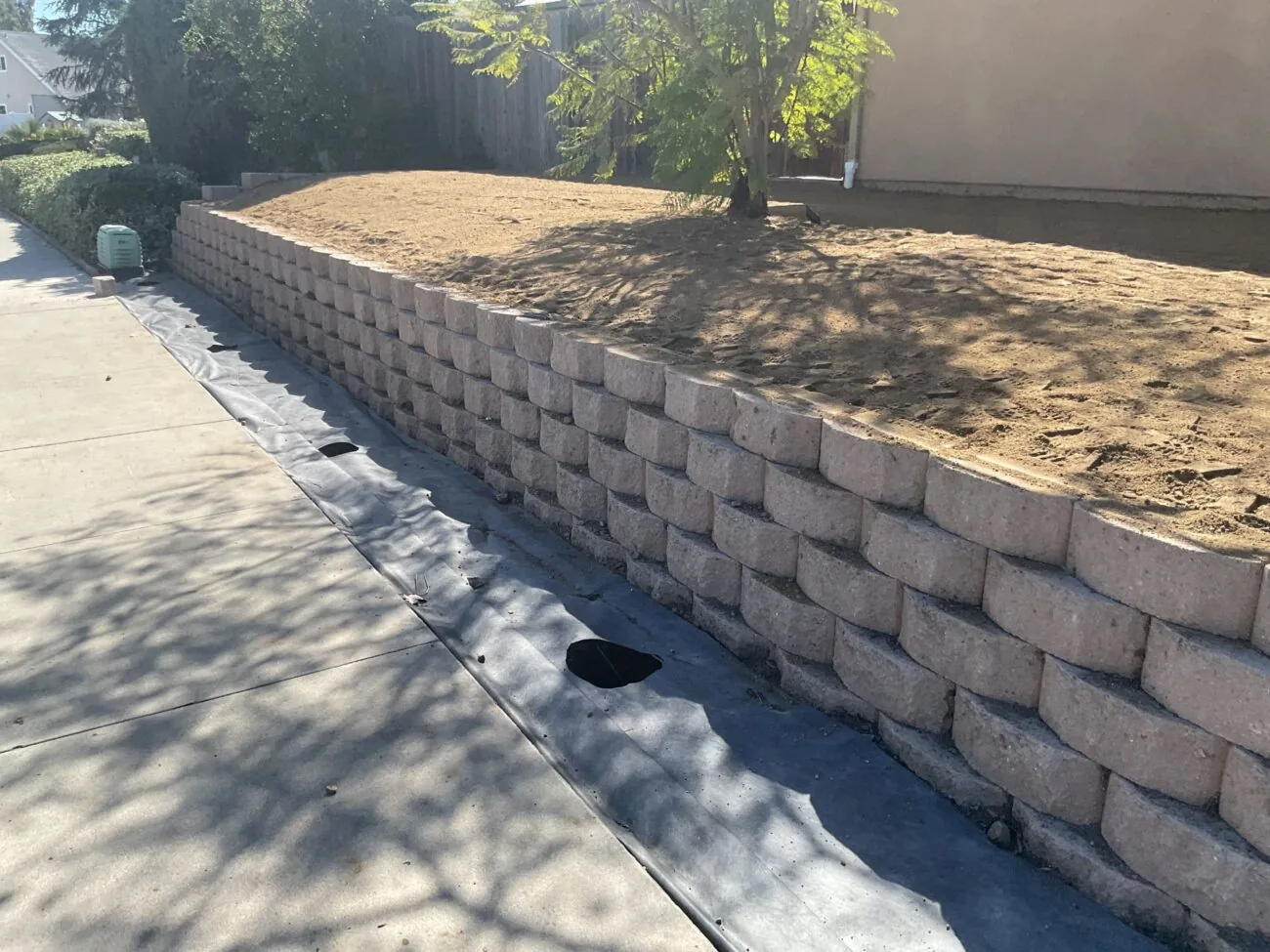 New block retaining wall along a sidewalk with graded fill behind it, retaining walls