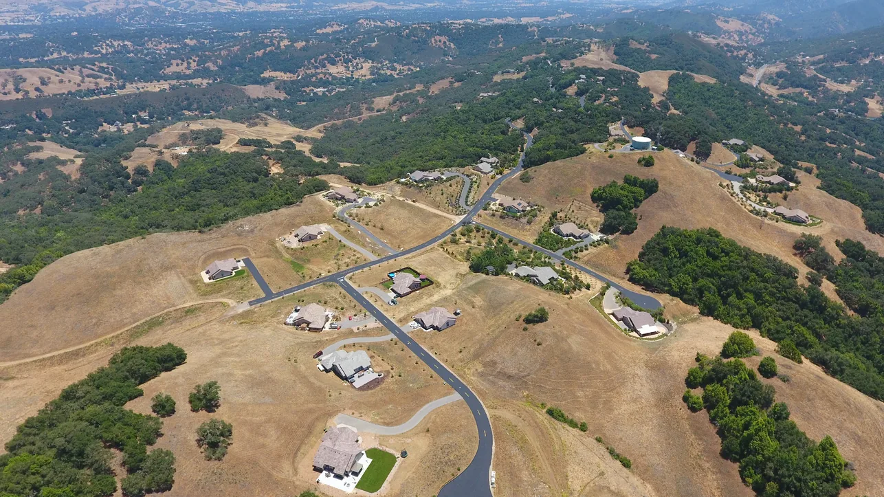 Aerial view of homes and winding paved roads across golden hills dotted with oaks